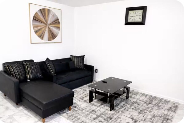 Uma sala de estar moderna com um sofá seccional, uma mesa de centro, um relógio de parede e uma pintura abstrata emoldurada.