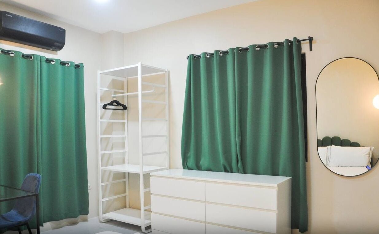 Een kamer met een witte kast, een spiegel en groene gordijnen.