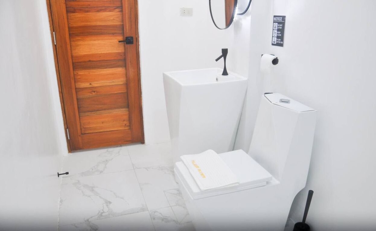 A bathroom with a wooden door, a white sink, a toilet, and a shower area.