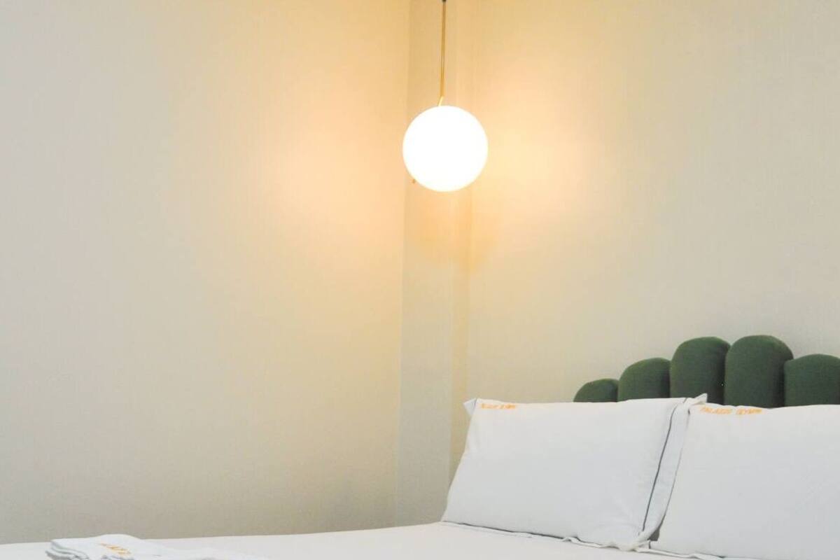 Une chambre d’hôtel avec un lit, un luminaire rond et une tête de lit verte.