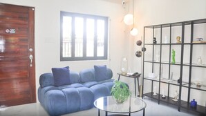 Ein Wohnzimmer mit einem blauen Sofa, einem Glastisch und einer schwarzen Regaleinheit mit Dekoration.