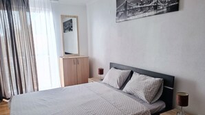A hotel room with a large bed, wooden wardrobe, bedside tables, and a cityscape painting on the wall. - Comfortable Apartment With sea View (Bar)