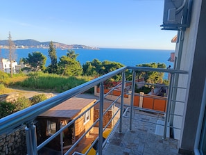 A balcony with a metal railing overlooking a coastal area with buildings and a clear view of the sea. - Comfortable Apartment With sea View (Bar)