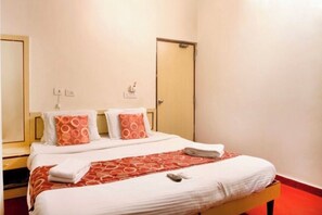 A hotel room with a bed, two pillows, a blanket, a bedside table, and a door. - Hotel royal inn (Hyderabad)