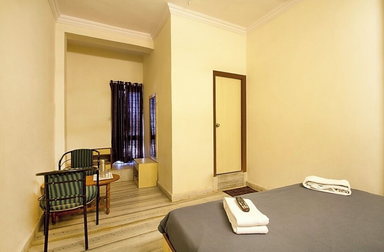 A hotel room with a bed, a chair, a small table, a mirror, and a window with curtains.