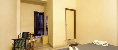 A hotel room with a bed, a chair, a small table, a mirror, and a window with curtains.
