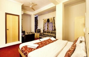 A hotel room with a bed, a television, a sofa, and curtains. - Hotel royal inn (Hyderabad)