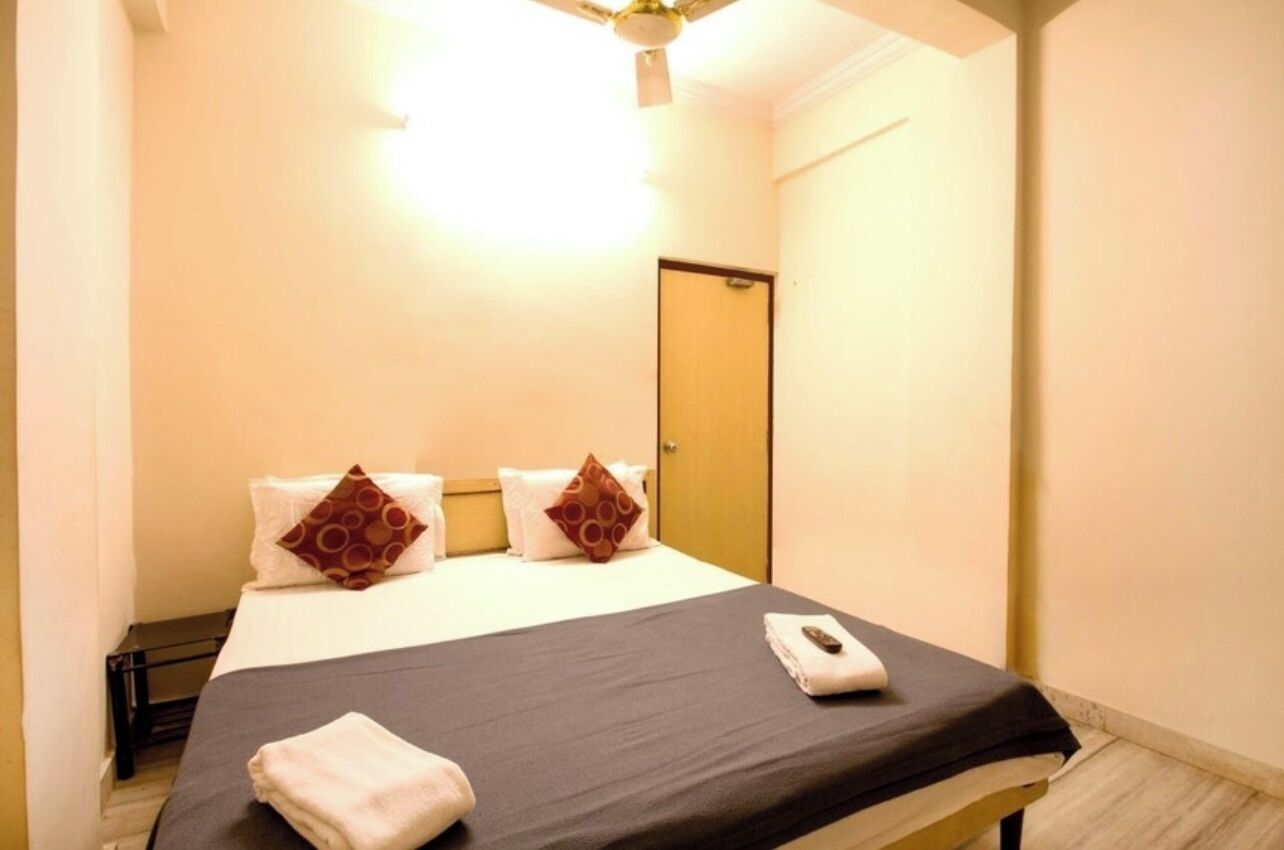 A hotel room with a bed, a bedside table, a remote control, and a door.