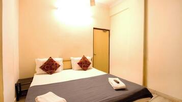 A hotel room with a bed, a bedside table, a remote control, and a door.