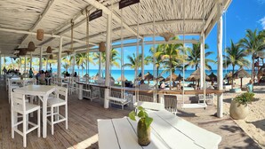 Un restaurant situé en bord de mer, avec une terrasse, des palmiers et une vue sur l’océan.
