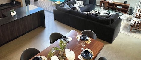 A modern living space with a dining area, a sofa, a TV, and a kitchen.