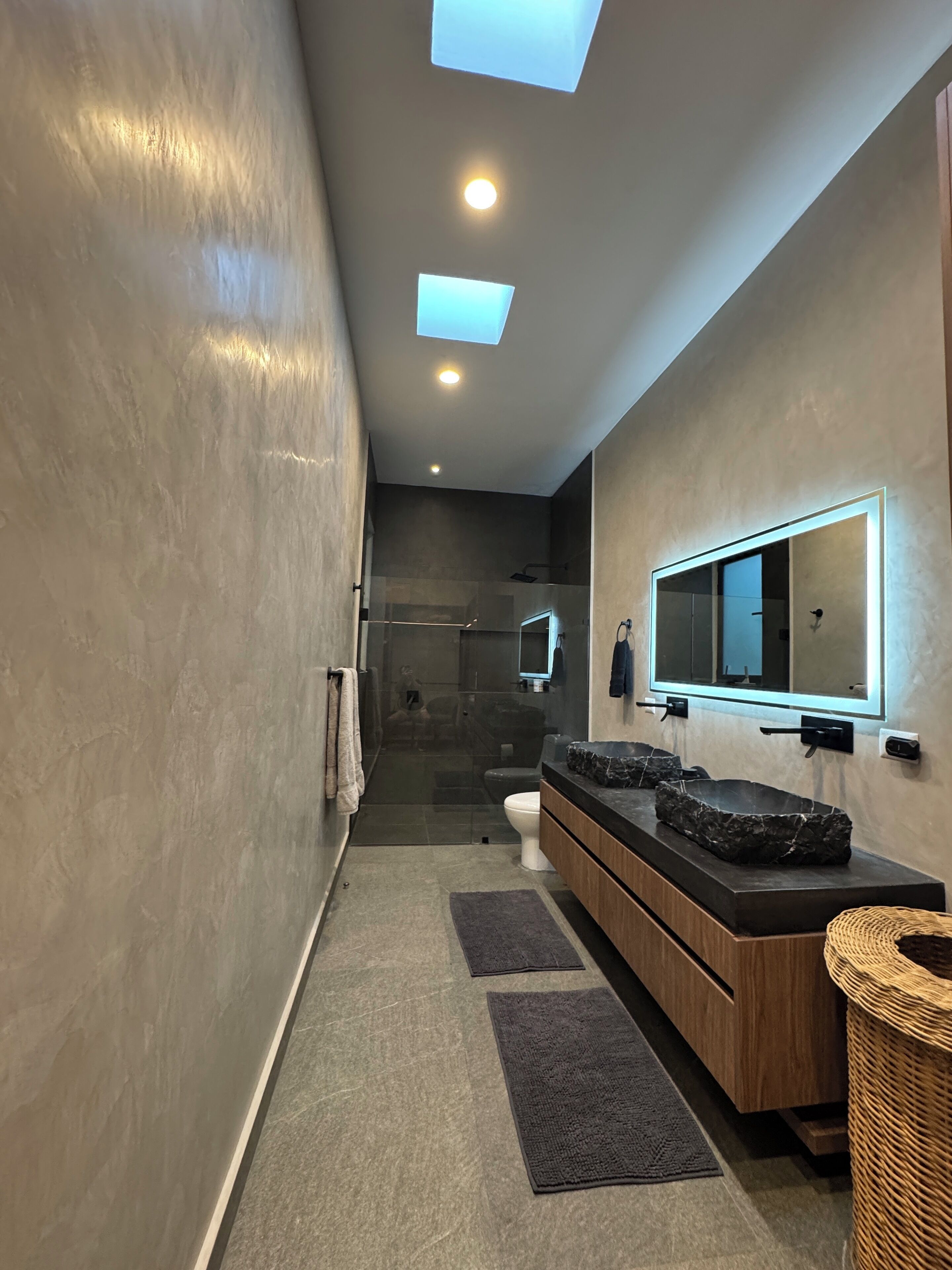 Une salle de bain moderne dotée d’une douche à parois de verre, d’un meuble-lavabo en bois avec un grand miroir et d’une douche à l’italienne.