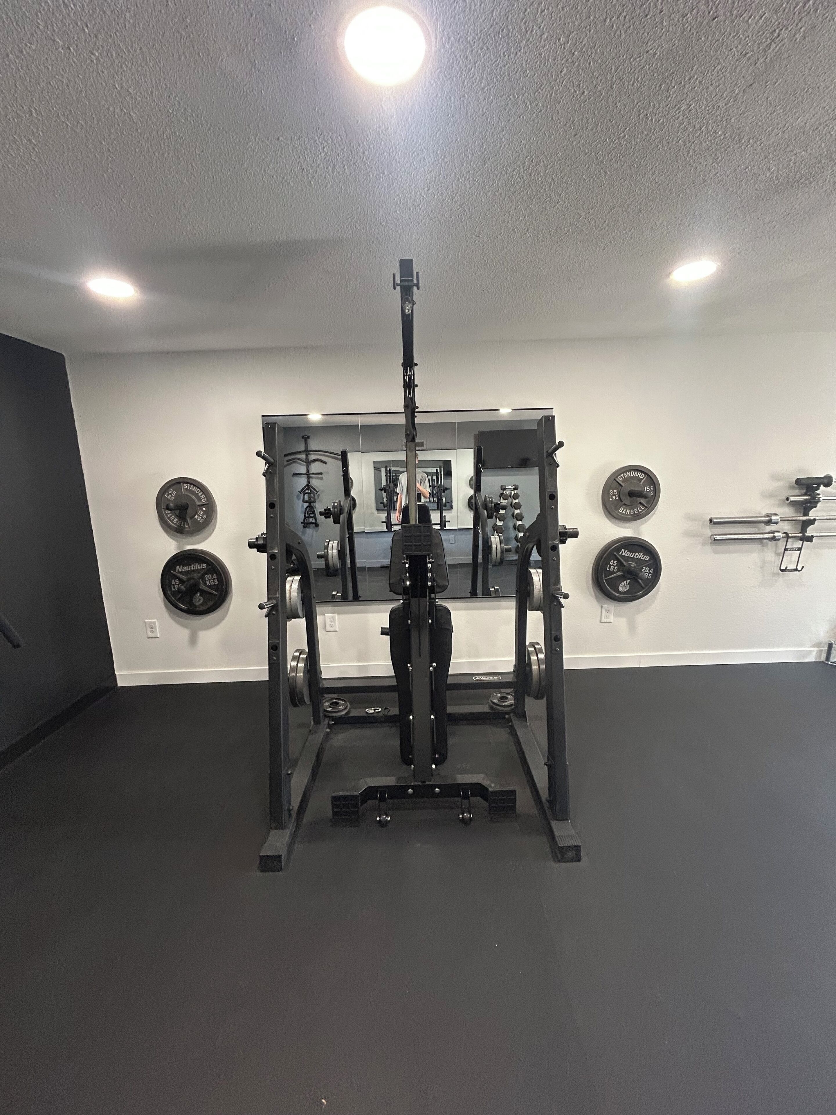 Ein Fitnessraum mit Squat-Stange, Gewichte und einem Spiegel an der Wand.