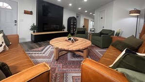 Un soggiorno moderno con una televisione a schermo piatto, due poltrone verdi, un tavolino in legno e un tappeto decorato.