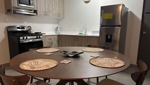 Uma cozinha moderna com uma mesa de jantar redonda, cadeiras de madeira, micro-ondas, fogão e geladeira.