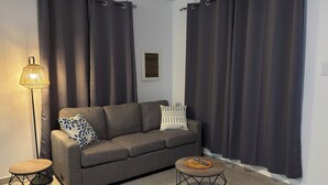 Uma sala de estar moderna com um sofá cinzento, duas mesas laterais a combinar e cortinas escuras.