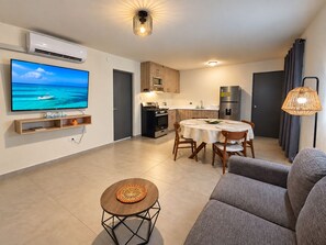 Un salon moderne comprenant un téléviseur à écran plat, une table à manger avec des chaises, un canapé et une petite table basse.