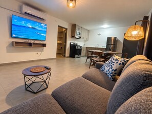 A modern living room with a flat-screen TV, a dining area, and a kitchen.