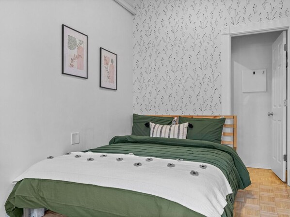 Quarto com cama, roupa de cama verde, duas quadros na parede e uma porta para outro cômodo.