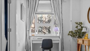 Een slaapkamer met een bed, een bureau met stoel, een raam met gordijnen en een nachtkastje met lamp en plant.