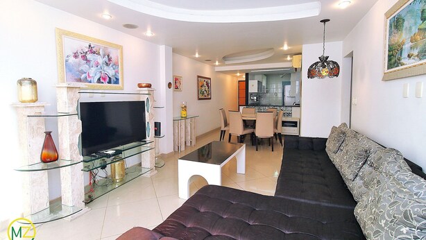 Una sala de estar moderna con un televisor de pantalla plana, una mesa de centro de vidrio y un sofá oscuro.