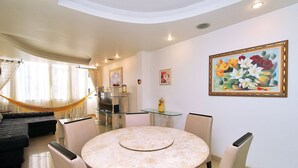 Un comedor con una mesa redonda y sillas, una hamaca y una zona de cocina con armarios y un refrigerador.