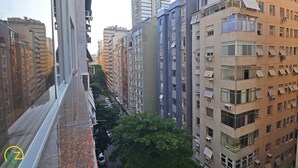Un edificio residencial de varios pisos con balcones, una calle estrecha y un árbol en primer plano.