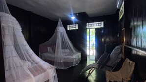 Una habitación tenuemente iluminada con dos camas cubiertas por doseles blancos, suelo de madera y un gran ventanal que deja entrar luz natural.