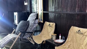 Una habitación con paredes de madera oscura, una ventana con persianas, un ventilador de techo y dos sillas con una mesa.