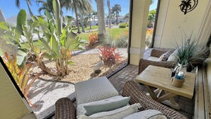 A sunlit patio with wicker furniture, a small table with a vase, and a view of a landscaped garden with palm trees. - TOP FLORIDA's Villa Pelican Point (Cape Coral)