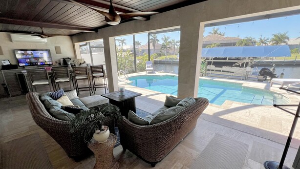 A spacious living area with a large pool, wicker furniture, and a television. - TOP FLORIDA's Villa Pelican Point (Cape Coral)