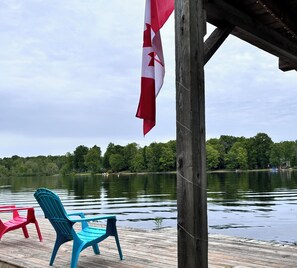 Une jetée en bois avec des chaises, un drapeau et un lac bordé d’arbres en arrière-plan.