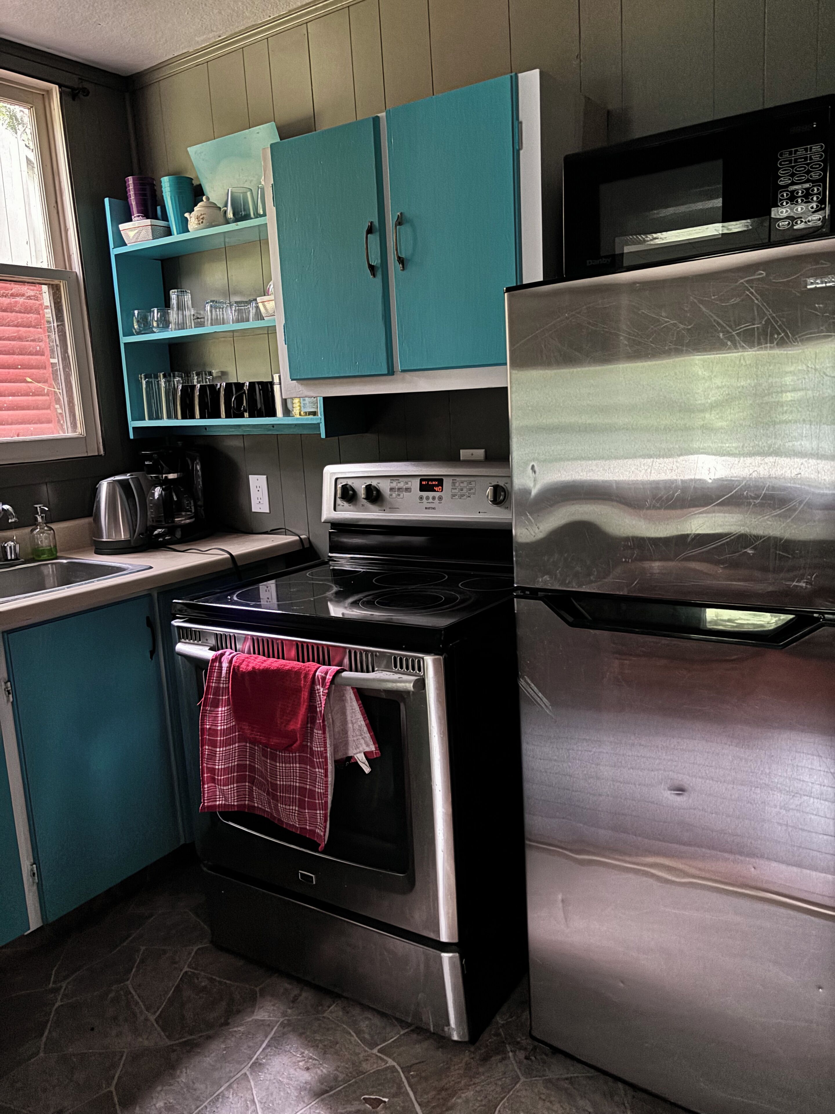 A kitchen with teal cabinets, a stainless steel oven, a microwave, and a coffee maker.