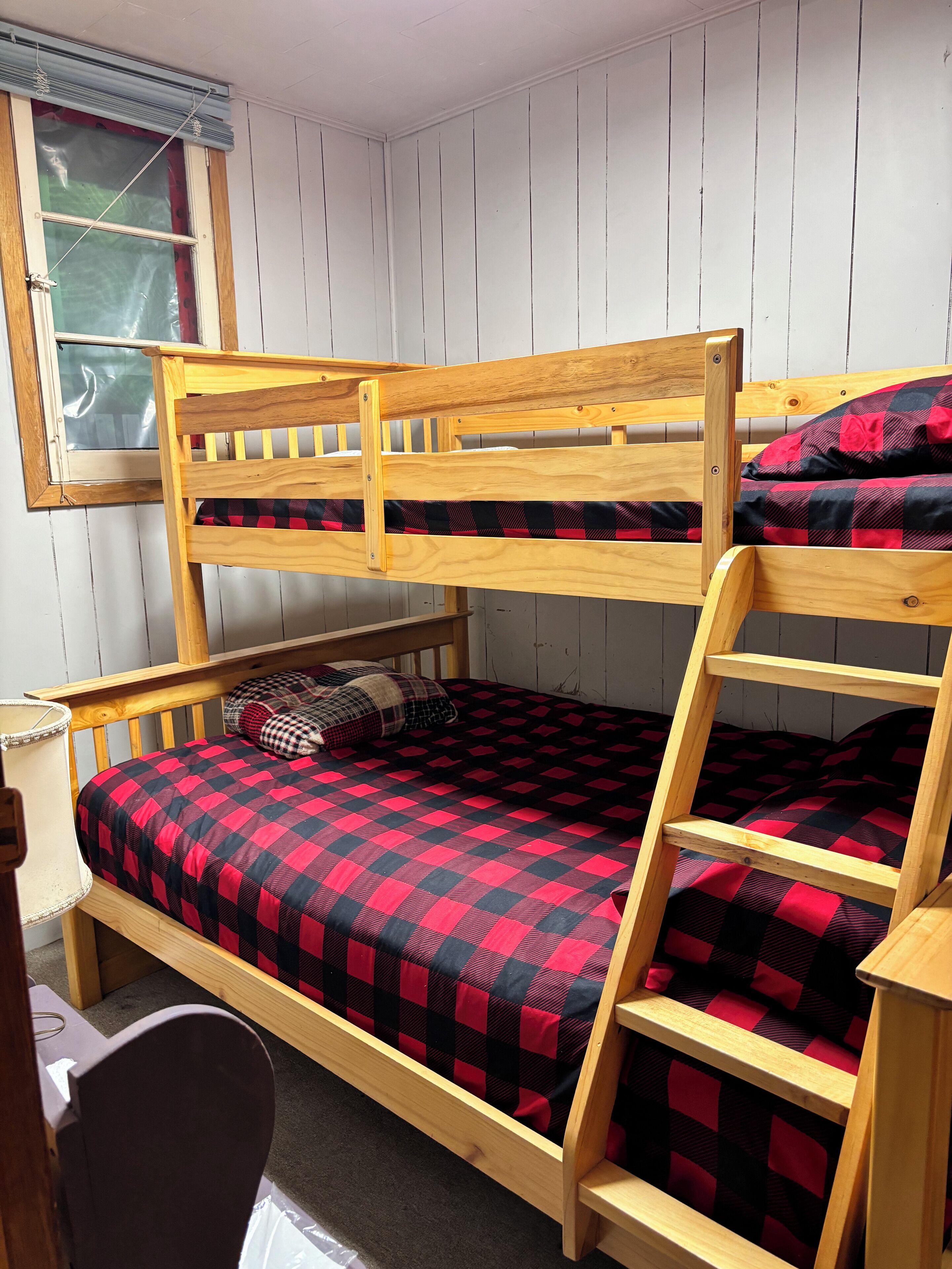 A bunk bed with a checkered blanket, a window with blinds, and a wooden desk.