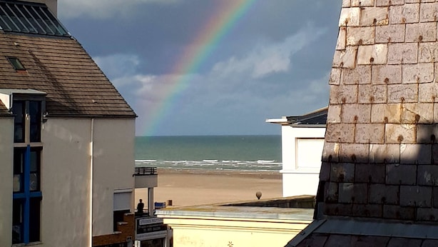 Un bâtiment doté d’un toit en pente, avec un arc-en-ciel visible en arrière-plan.