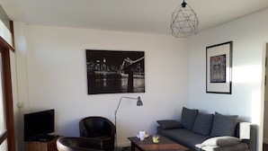 Un salon avec un canapé, des fauteuils, une table basse, un téléviseur et un tableau.