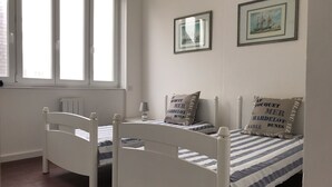 Une chambre avec deux lits simples, une fenêtre et deux tableaux encadrés accrochés au mur.