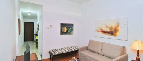 Una sala de estar con sofá, mesa de centro, televisor y lámpara.