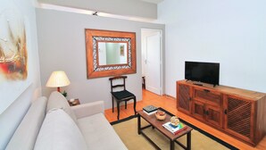 A living room with a sofa, a coffee table, a TV on a wooden cabinet, a lamp, and a mirror on the wall. - Nossa Senhora VII (Rio de Janeiro)