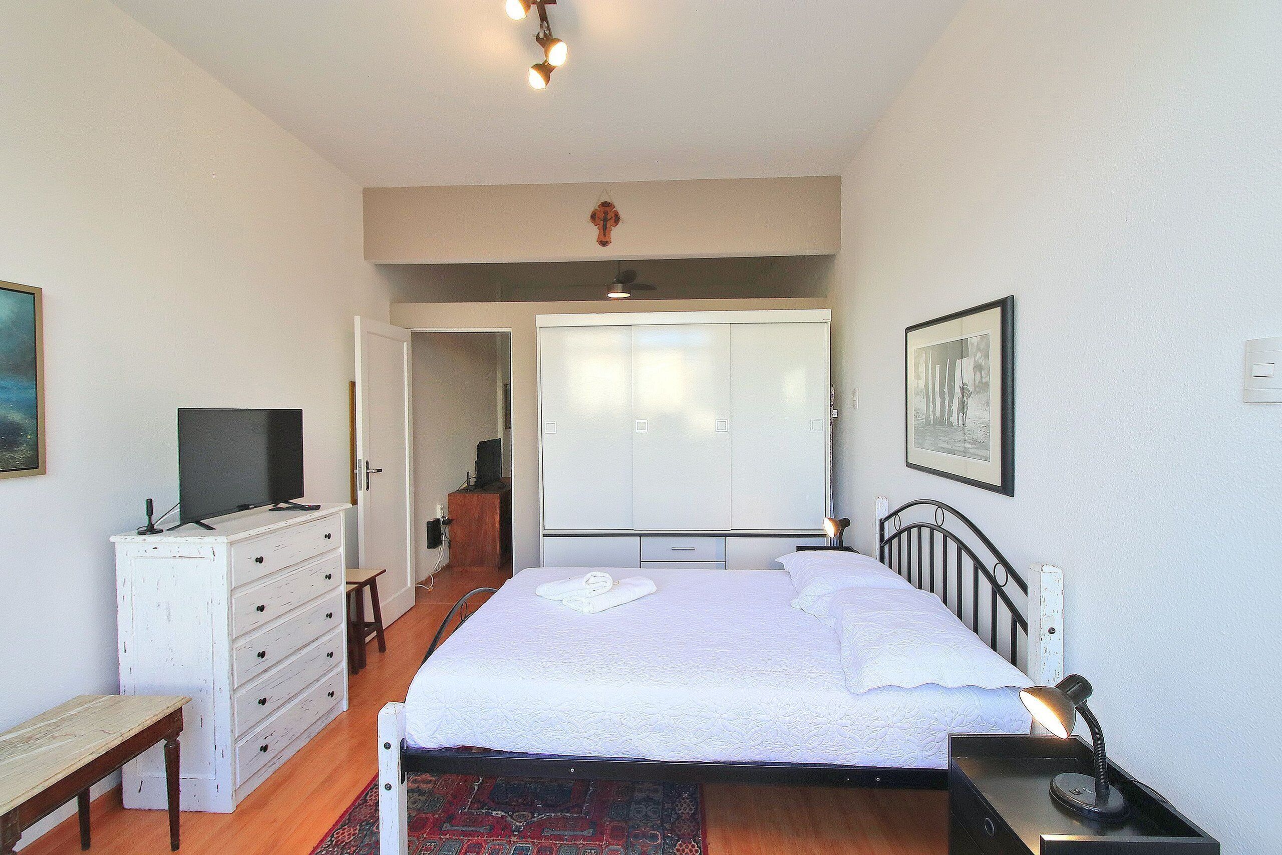 Un dormitorio con cama, mesita de noche, escritorio, armario y televisor.