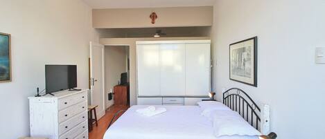 Un dormitorio con cama, mesita de noche, escritorio, armario y televisor.