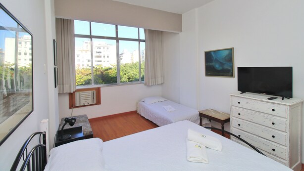 A hotel room with two beds, a TV, a dresser, and a window with a city view. - Nossa Senhora VII (Rio de Janeiro)