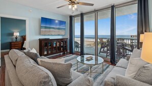 Un salon spacieux doté d’une grande fenêtre donnant sur la plage, d’un ventilateur de plafond et d’un coin salon confortable.