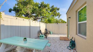 Un jardin avec une table de pique-nique, des chaises, un tuyau d’arrosage et une clôture blanche.