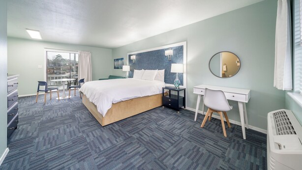 Habitación de hotel con cama, escritorio, silla y un ventanal con cortinas.