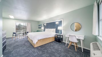 A hotel room with a bed, desk, chair, and a large window with curtains.