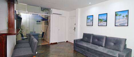 A reception area with a grey sofa, a wooden chair, and a glass partition. There are three framed pictures on the wall.