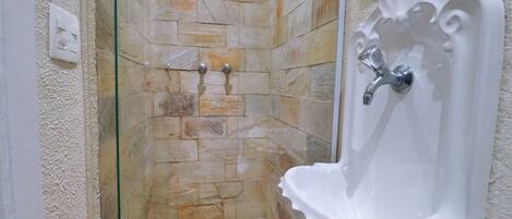 Un baño con ducha envuelta en vidrio, baldosas de piedra y un lavabo blanco con un diseño decorativo.
