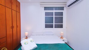 Ein Hotelzimmer mit Bett, Fenster, Klimaanlage, Holzschrank und einem Handtuch mit Logo.