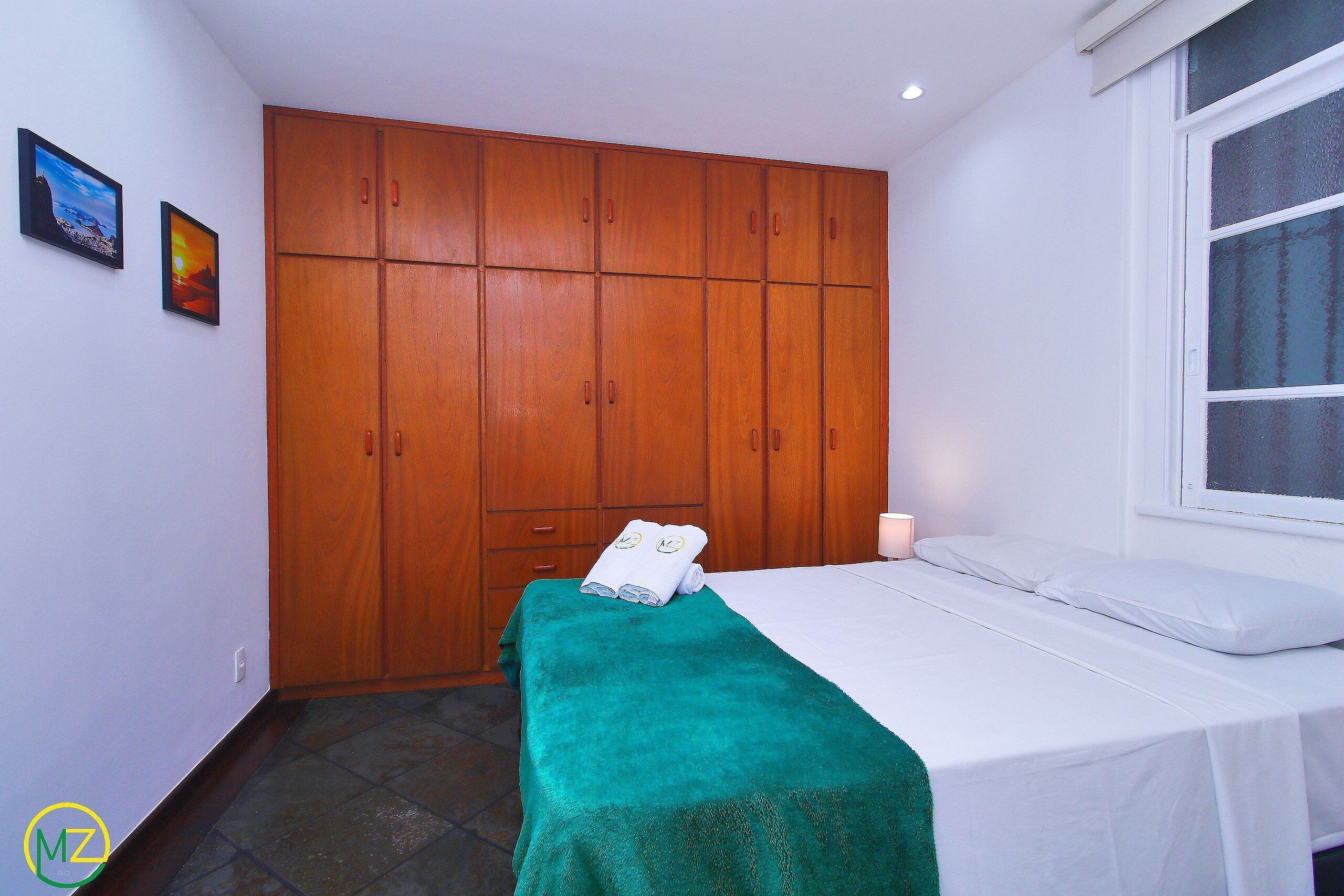 Ein Hotelzimmer mit einem Bett, einem grünen Handtuch, einem Holzschrank und einem Fenster.